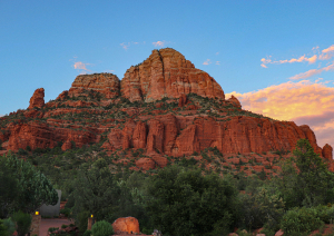 массивная красная гора на фоне голубого неба с облаками, а внизу зеленая растительность